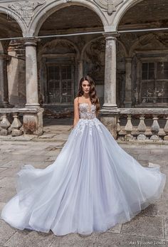 a woman in a white wedding dress standing on the ground with an old building behind her