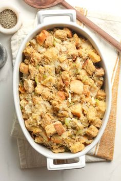 a casserole dish filled with stuffing on top of a white table next to wooden spoons