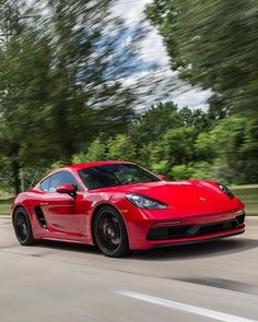 a red sports car driving down the road with trees in the backgrouund