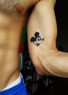 a man with a mickey mouse tattoo on his left arm and another person's right arm behind him