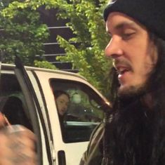 a man with long hair is holding something in his hand and looking out the car window