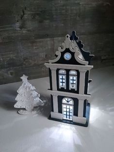 a black and white clock tower next to a small christmas tree on a snow covered table