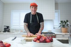 a man in an orange hat is cutting apples on a wooden board and smiling at the camera