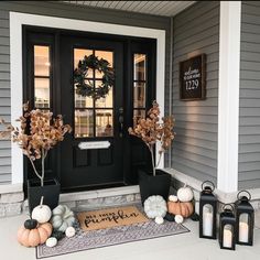 front porch decorated for fall with pumpkins, candles and wreath on the door mat