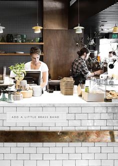 two people working behind the counter in a small restaurant with white tiles on the walls