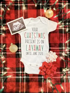 a baby's first christmas onesuit on a plaid blanket with ornaments around it