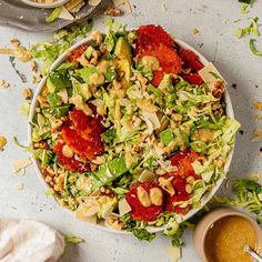 a salad with nuts, lettuce and tomatoes in a white bowl on a table