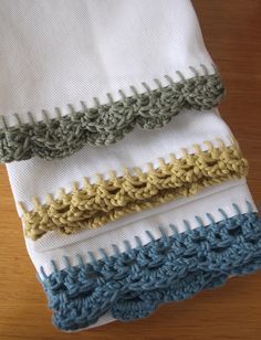 three different colored crocheted towels on top of a wooden table