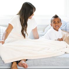 a woman sitting on top of a couch next to a little boy under a blanket