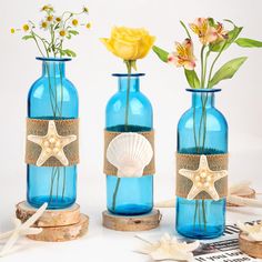 three blue vases with flowers and seashells in them on a table top