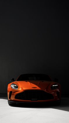 an orange sports car is parked in a dark room with its hood up and lights on