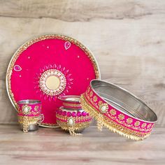 a pink and gold table setting with two silver dishes, one serving tray and the other sitting on a wooden surface