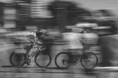 blurry photograph of three bicyclists riding down the street in black and white