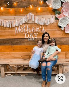 a woman and two children sitting on a bench in front of a wooden sign that says mother's day