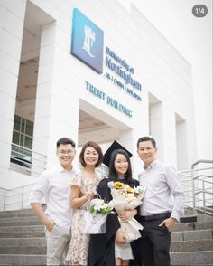 four people standing in front of a building holding bouquets and smiling at the camera