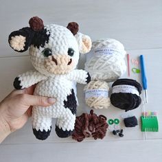 a hand holding a stuffed cow next to yarn and scissors