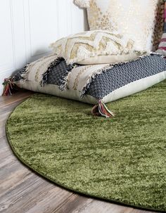 a green rug on the floor in front of a bed with pillows and throw pillows