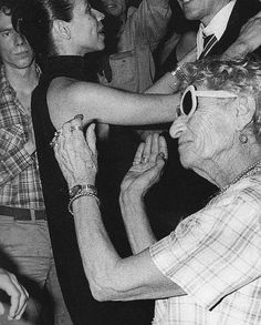 an older woman is dancing with a young man in the middle of a crowded room