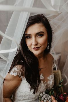 a woman in a wedding dress holding a bouquet under a sheer white veil with flowers on it