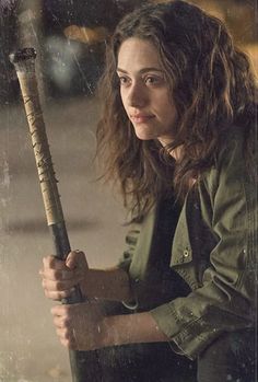 a woman holding a baseball bat in her hand and looking at the camera with an intense look on her face