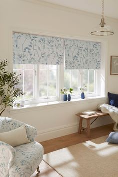 a living room filled with furniture and windows covered in blue floral roman blind shades on the windowsill