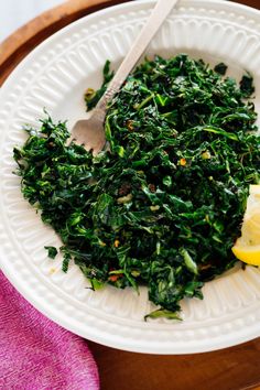 a white plate topped with spinach and lemon wedges on top of a wooden table