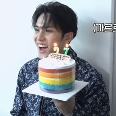 a man holding a cake with two candles on it