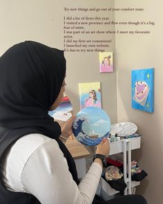 a woman sitting at a desk with a plate in her hand and some pictures on the wall behind her