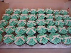 a box filled with cupcakes covered in blue frosting and white ribbon bows