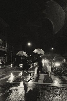 black and white photograph of people walking in the rain at night with umbrellas over their heads