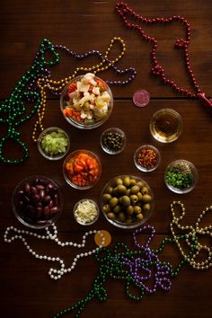 several bowls filled with different types of food on a wooden table next to beaded necklaces