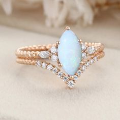 a white opal and diamond ring set on top of a beige cloth with flowers in the background