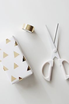 a pair of scissors next to a gift wrapped in white paper and gold foil tape