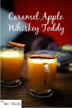 two glasses filled with orange liquid and cinnamon on top of a wooden table next to a book