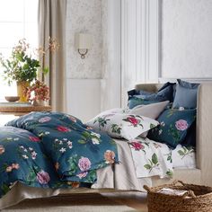 a bed covered in blue and pink flowers next to a basket filled with potted plants