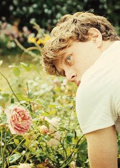 a young man in a field of flowers looking at the camera with an angry look on his face