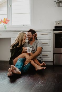 a man and woman sitting on the floor in front of an oven holding each other