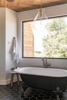 a bathroom with a claw foot bathtub next to a large window that looks out onto the trees