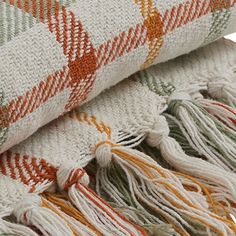 an orange, green and white blanket laying on top of each other with tassels