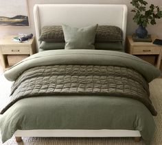 a bed with green comforter and pillows in a room next to two nightstands