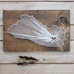 a string art piece sitting on top of a wooden table next to a dried flower