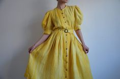 Vintage rustic yellow linen folk dress with puff sleeves, from the 1980s era Women's linen peasant dress with in shades of yellow, mid calf length, short puffy sleeves with pleats on the cuffs, buttoned front with gold plastic buttons, high waist and two pockets. The dress has a detachable belt and lining on the skirt. Made in Austria Material - 100% Linen, just the lining is synthetic Size on tag - 40 (EU) Model wears 38 EU or 8 US, fits slightly big in the bust area.  Approximate Measurements Vintage Linen Dress For Spring, Spring Vintage Linen Dress, Cottagecore Puff Sleeve Vintage Dress For Summer, Cottagecore Puff Sleeve Vintage Summer Dress, Cottagecore Vintage Puff Sleeve Dress For Summer, Cottagecore Vintage Puff Sleeve Summer Dress, Cottagecore Vintage Summer Dress With Puff Sleeves, Vintage Linen Dress For Spring Daywear, Fitted Linen Prairie Dress For Spring