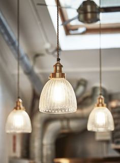 three glass lights hanging from a ceiling in a kitchen with exposed pipes and piping