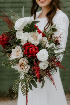 a woman holding a bouquet of white and red flowers with greenery in her hands