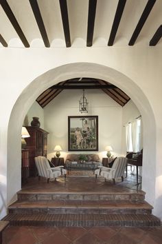 an archway leading to a living room with two chairs and a piano in the background