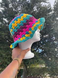 a hand holding up a crocheted hat on top of a mannequin head