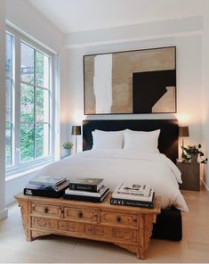 a bed with white sheets and pillows next to a large painting on the wall above it