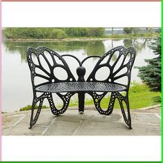 a black metal bench sitting on top of a stone walkway next to a lake with trees in the background