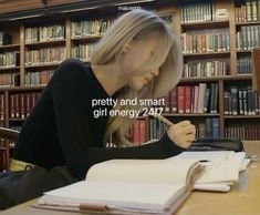 a woman sitting at a table in front of a book shelf with books on it