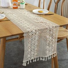 the table is set with plates and cups on it, along with a crocheted doily runner